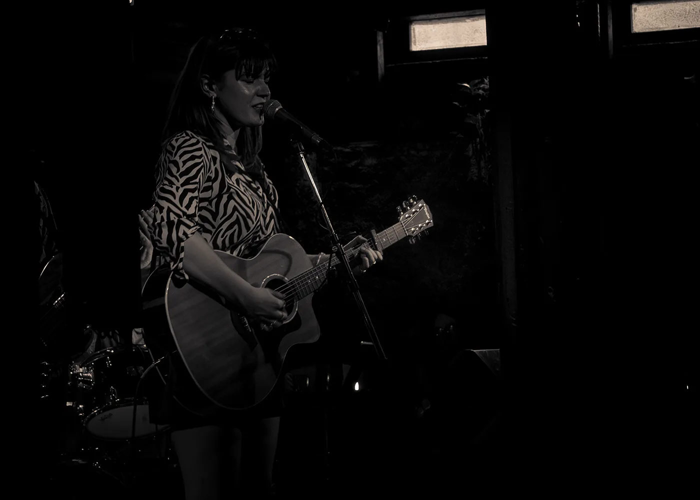 a singer in a patterned shirt playing an acoustic guitar at a microphone, in warm sepia light