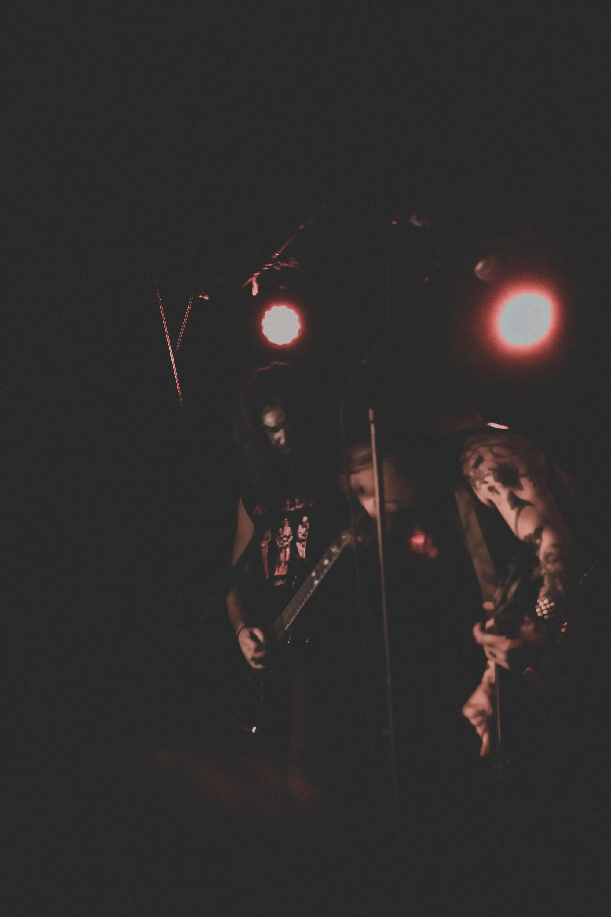 Two guitarists bowed under dim red house lights