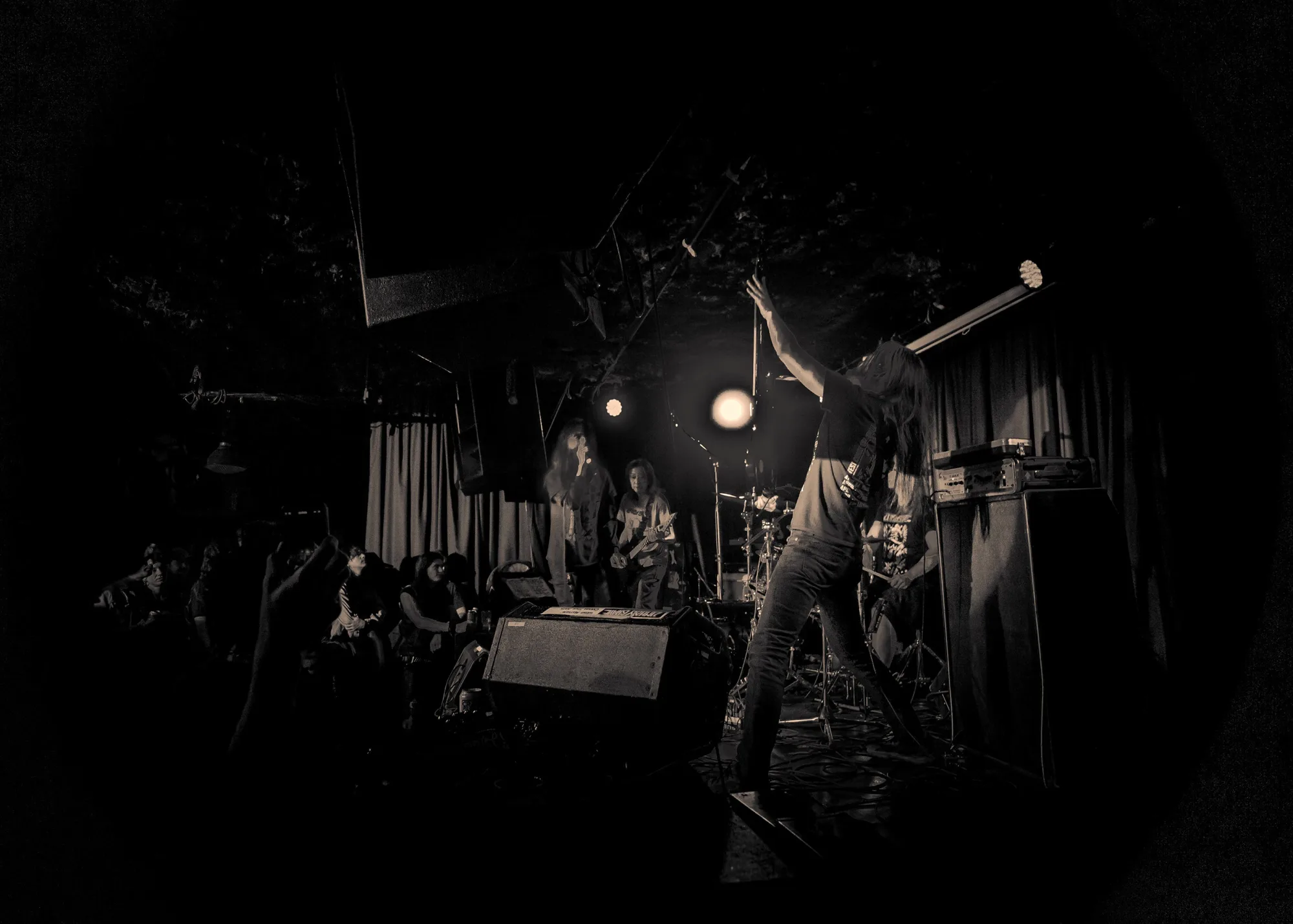 A performer raises an arm over a packed dive-bar stage in sepia dark