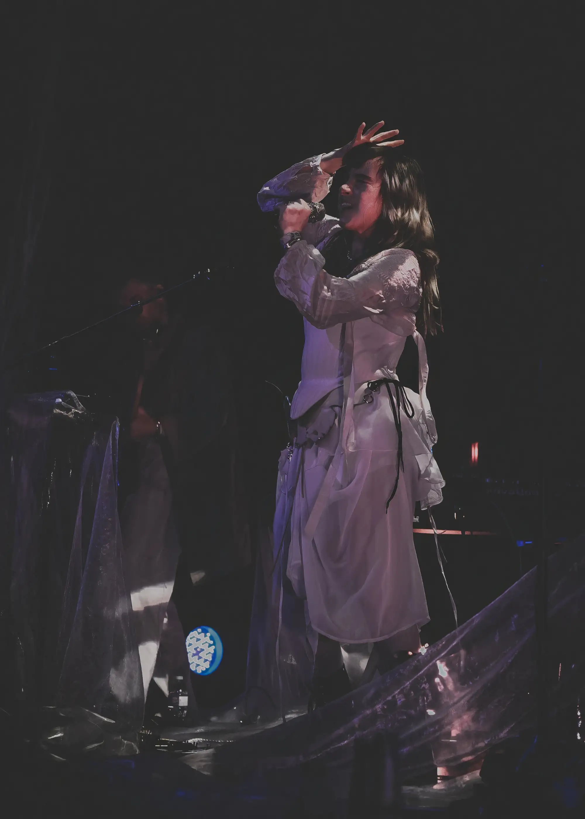 A singer in pale layered fabric shields her eyes in a beam of light