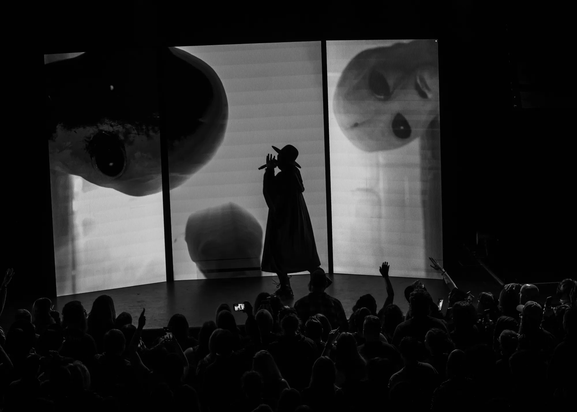A silhouetted singer flanked by monstrous faces projected on screens