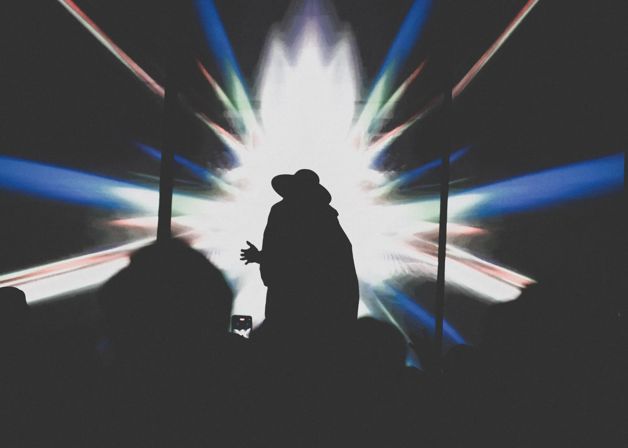A hatted silhouette stands before a white starburst of stage light
