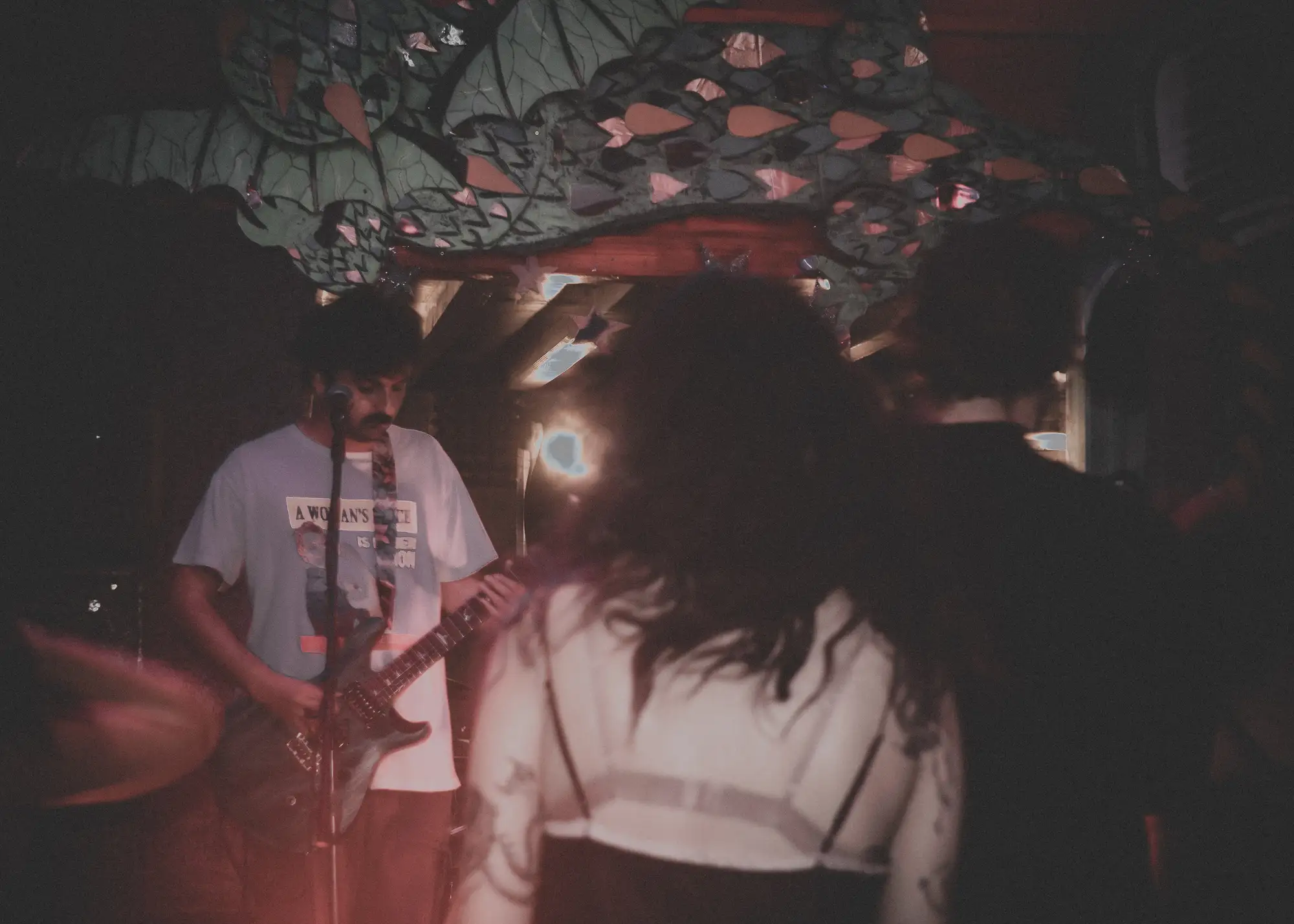 Dark grainy crowd facing a guitarist under a dragon stage prop