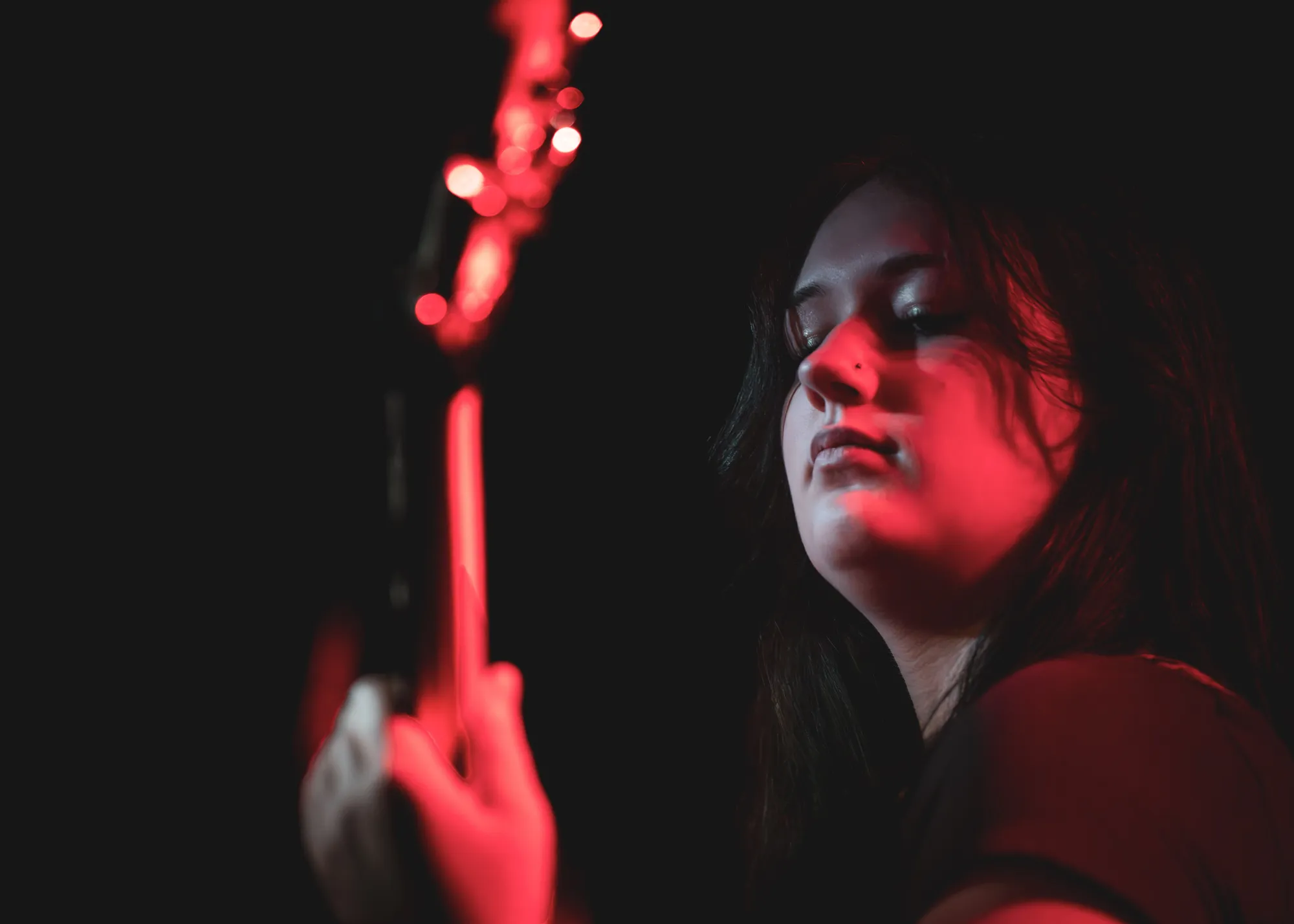 Bassist lit entirely in red, looking down the neck of the bass
